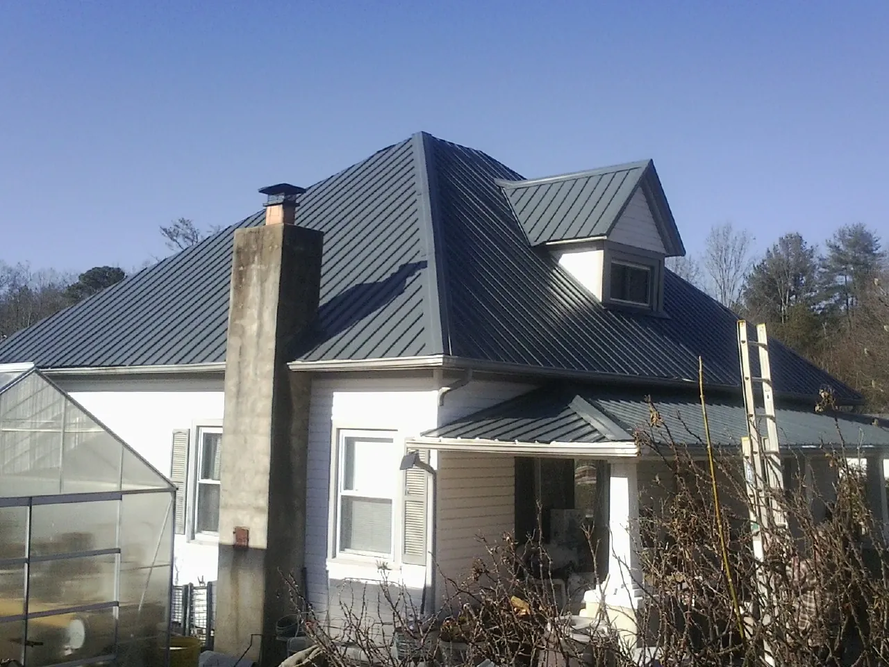 Dark blue standing seam metal roof on a white farmhouse with dormer — Slate & Tile Roof Repair by Roofing Brothers in North Fort Myers