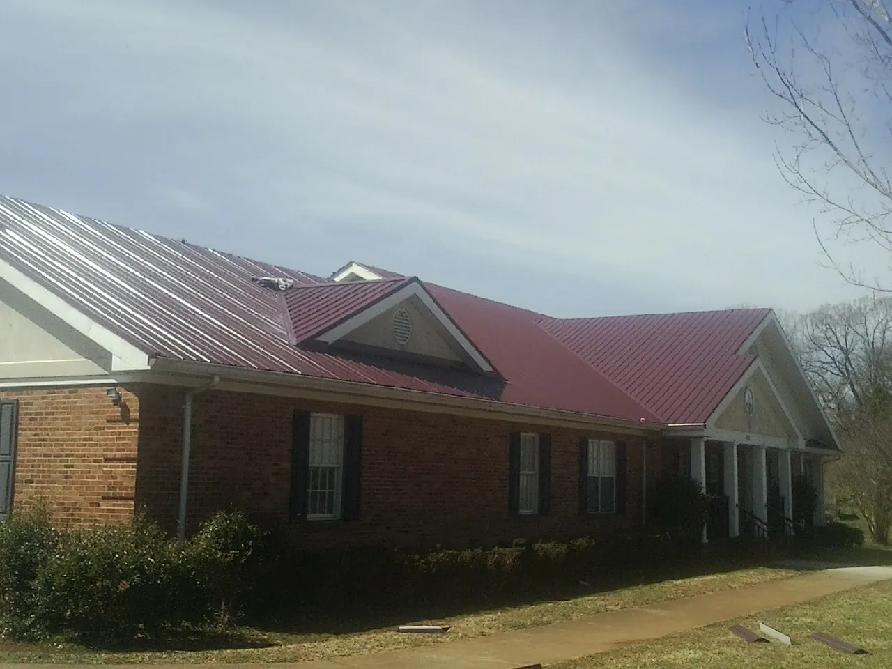 Red metal roof with gabled entries on a long brick building, from a Hail Damage Roof Repair job in North Fort Myers