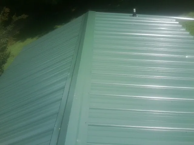 New green metal panels meeting at the ridge of a roof — Flat Roof Repair work by our crew in North Fort Myers