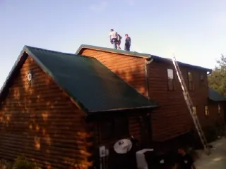 Crew on the ridge of a green metal roof on a two story log home in North Fort Myers