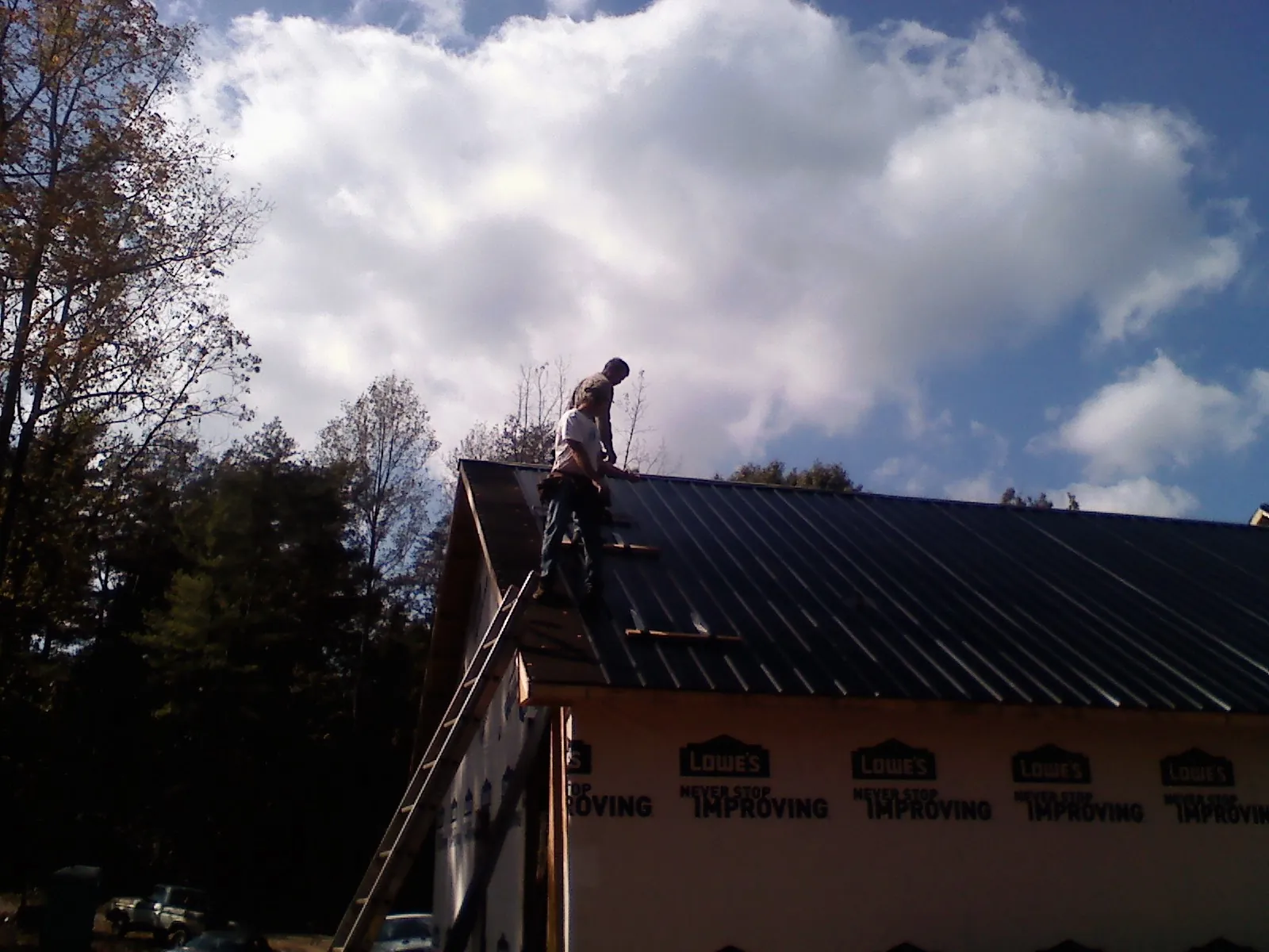Roofer fastening dark metal panels high against a cloudy sky, from a Roof Inspection job in North Fort Myers