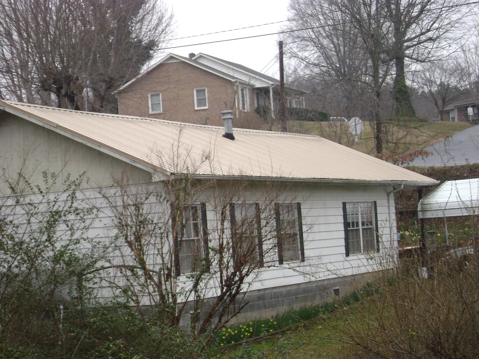 Tan metal roof on a white sided house set into a hillside — Commercial Roofing by Roofing Brothers in North Fort Myers